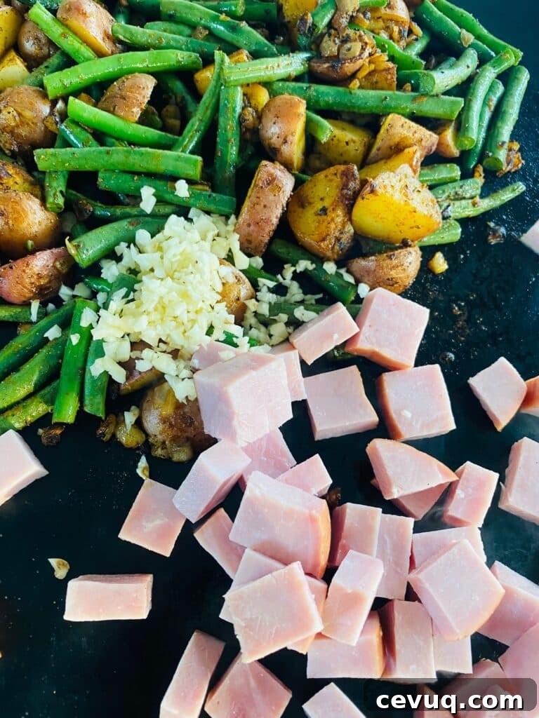 adding the ham and garlic to Blackstone Ham Potatoes and Green Beans