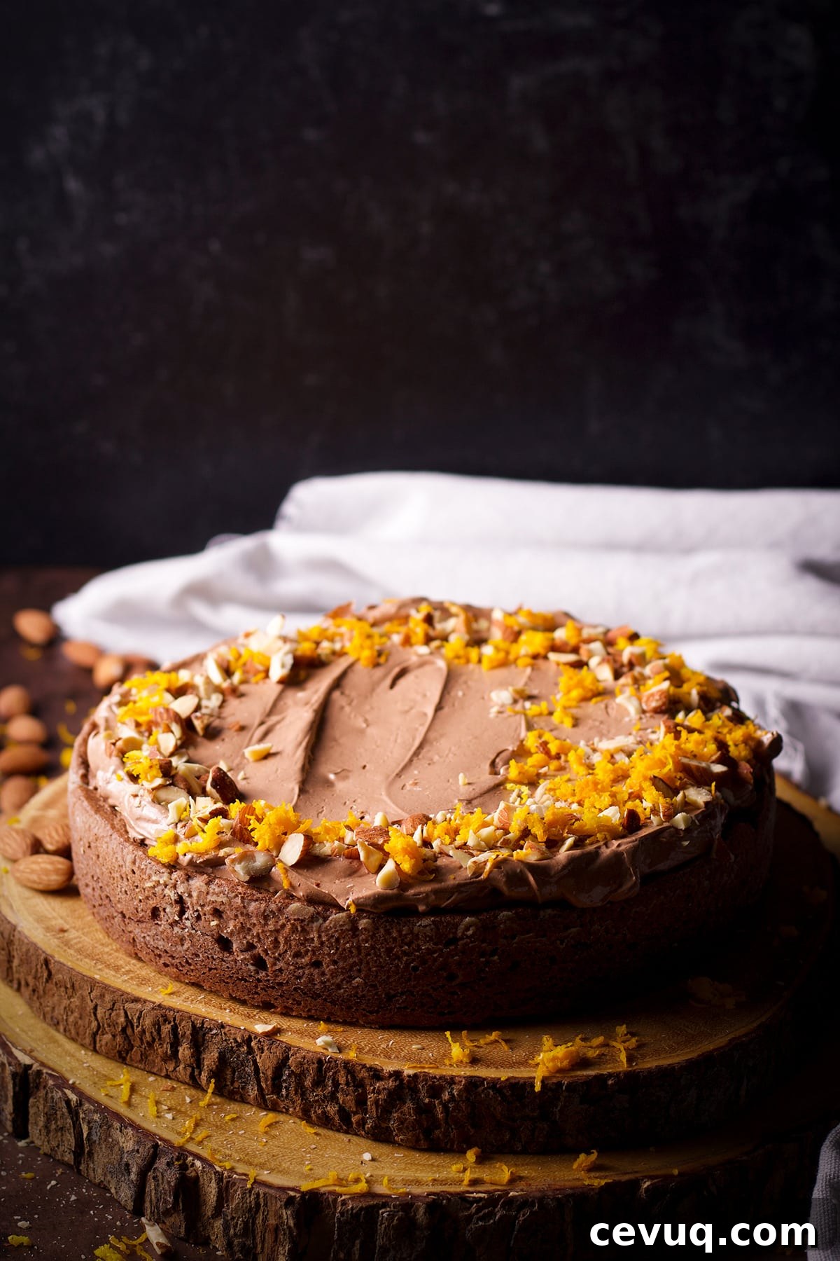 A one layer chocolate almond cake on a wood cake tray. The cake has been frosted with chocolate orange buttercream and decorated with chopped almonds and orange zest.
