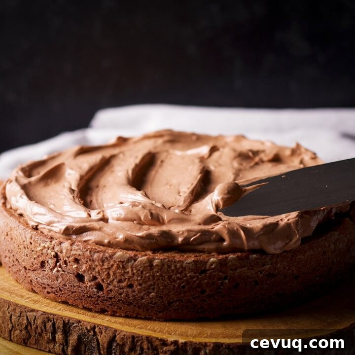 Someone using an icing spatula to spread chocolate orange buttercream over a chocolate cake.