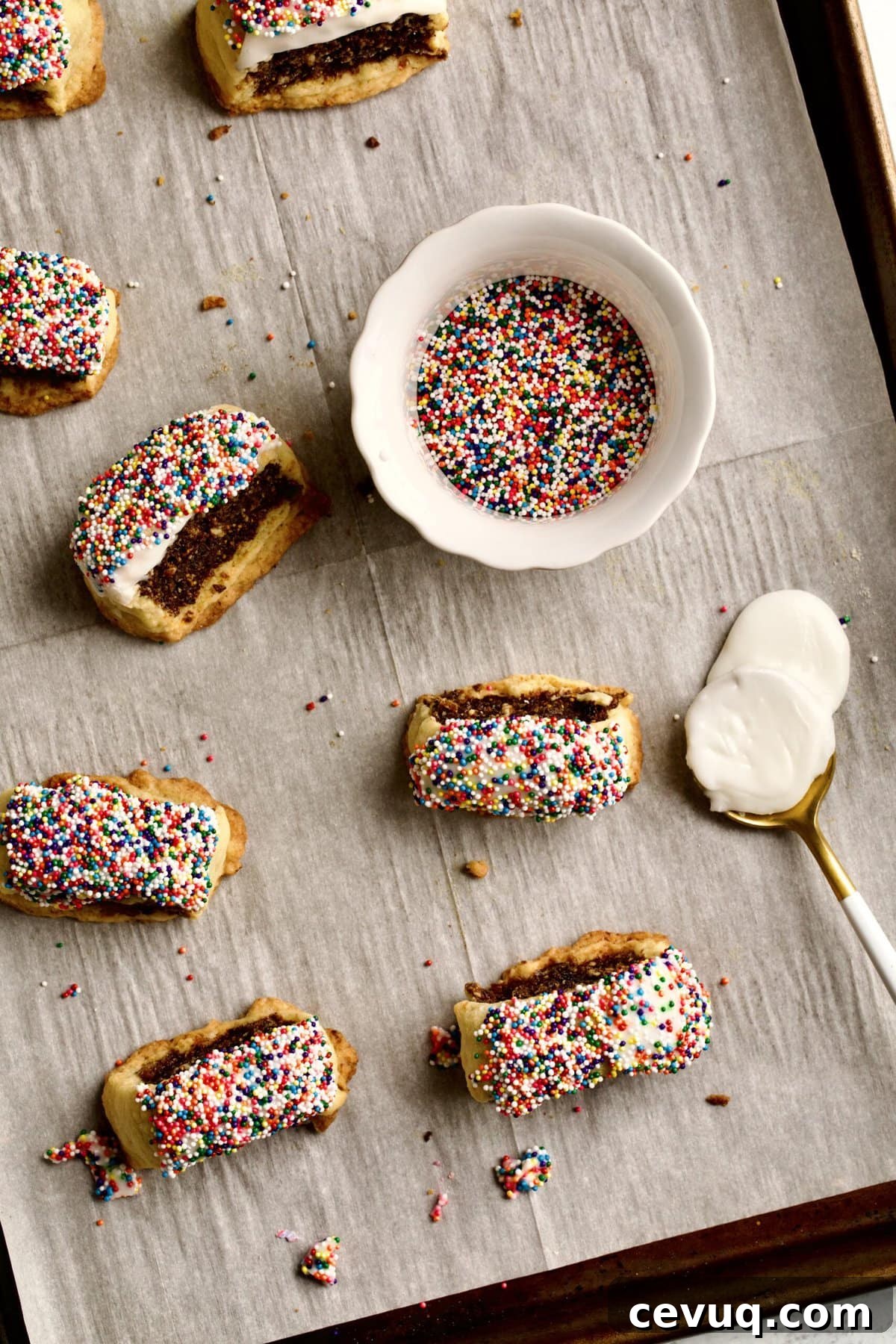 Italian fig cookies on baking sheet with glaze and sprinkles on the side to dip the cookies.