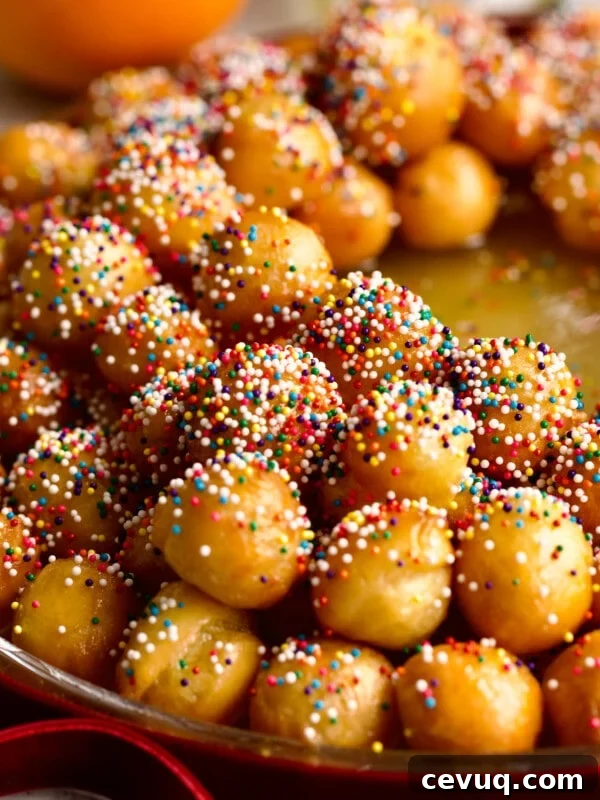 Struffoli honey dough balls with sprinkles on a serving platter in a wreath shape.