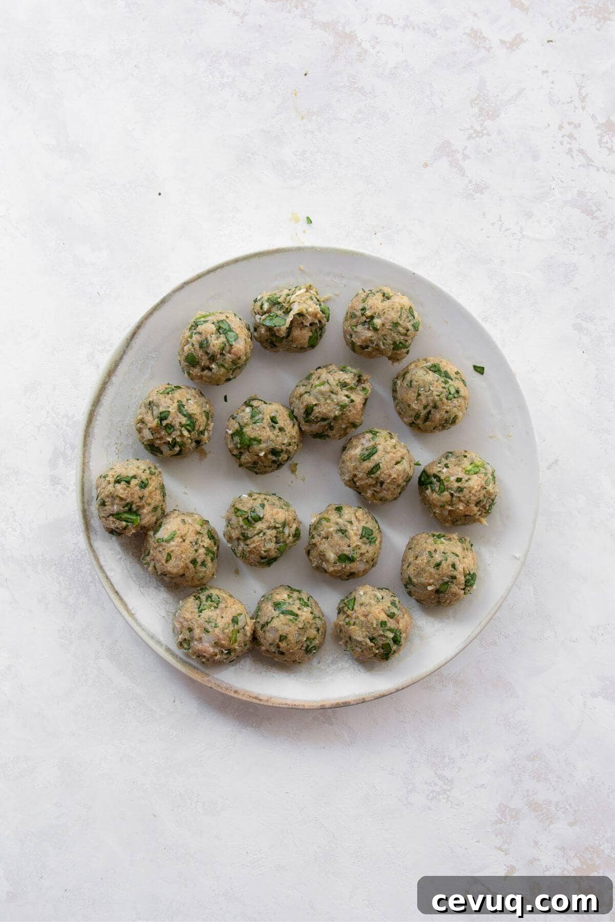 Uncooked chicken meatballs rolled and arranged on a plate, ready to be air fried.