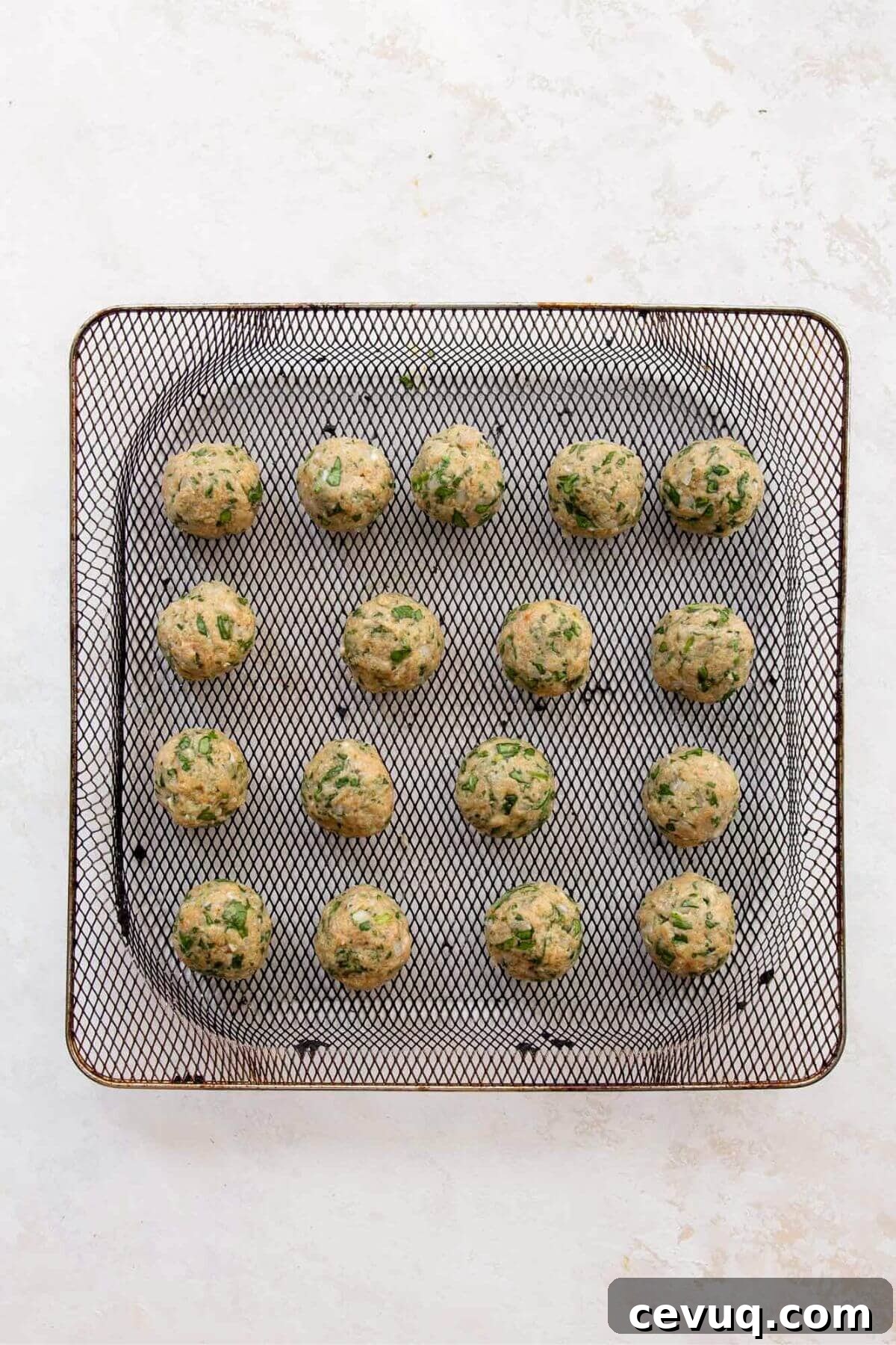 Uncooked chicken meatballs arranged in a single layer in an air fryer basket.