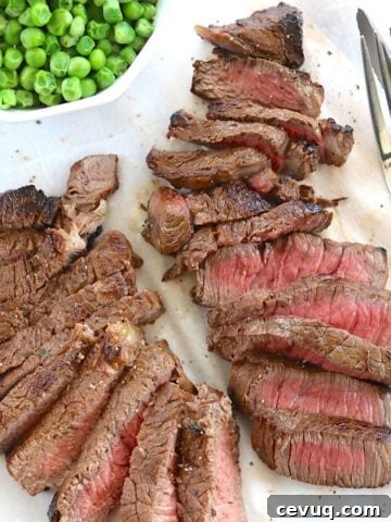 Sliced medium rare pink sirloin steak with a side of green peas.