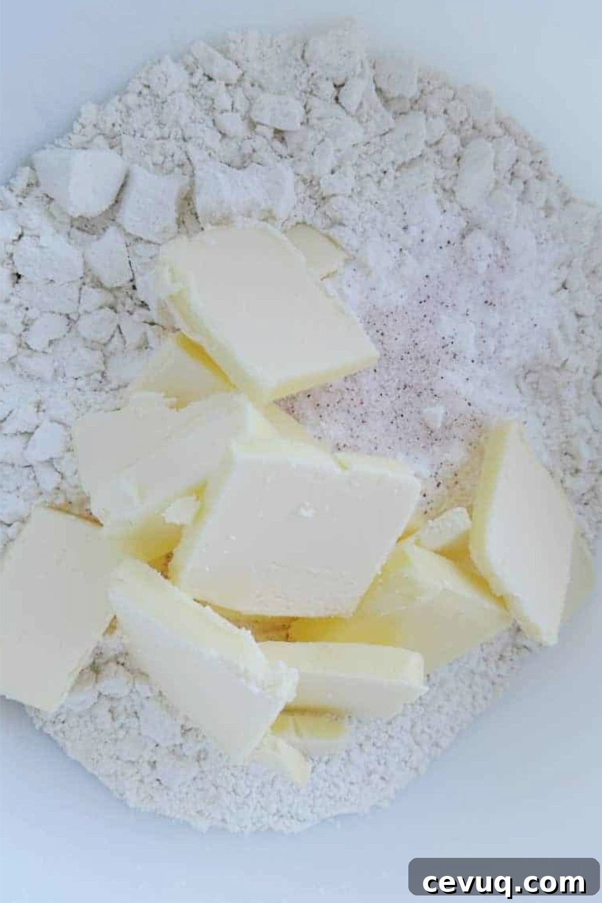 Flour, baking powder, and salt in large bowl with butter pieces on top.