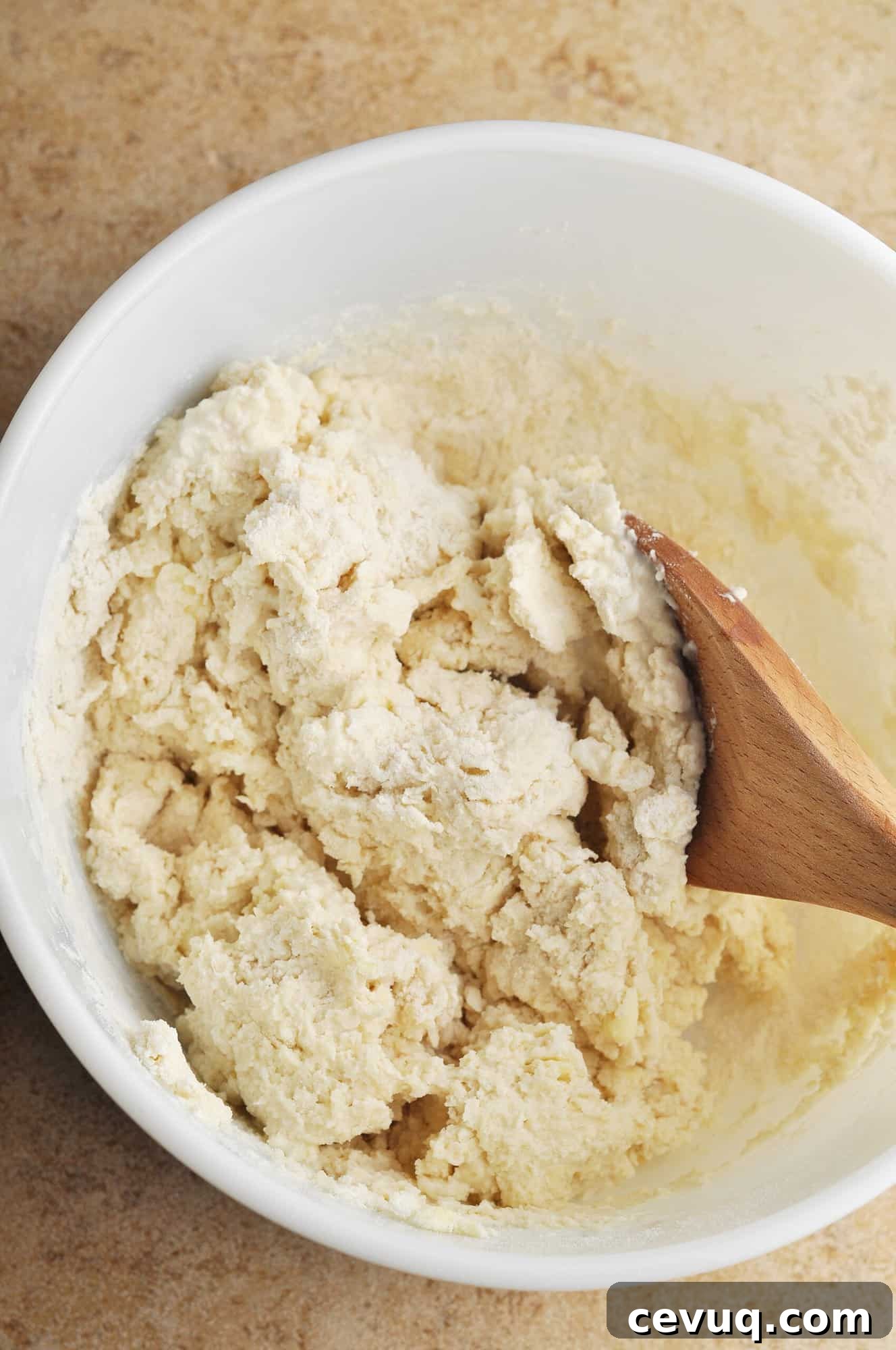 Biscuit dough in large bowl with wooden spoon.