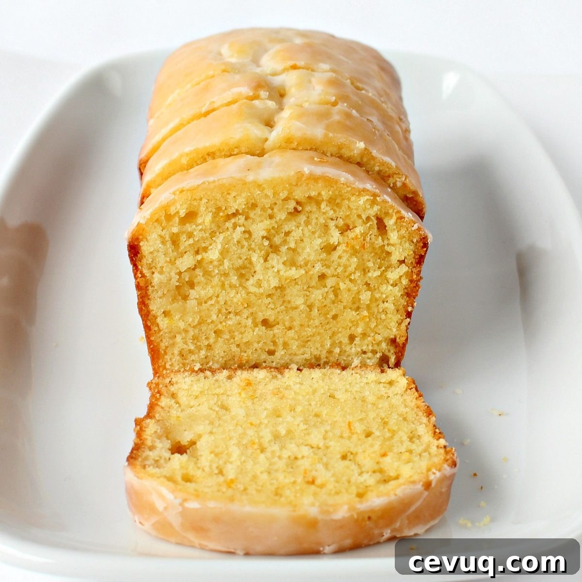 Close up of loaf with lemon yellow slice of cake topped with light yellow lemon glaze.