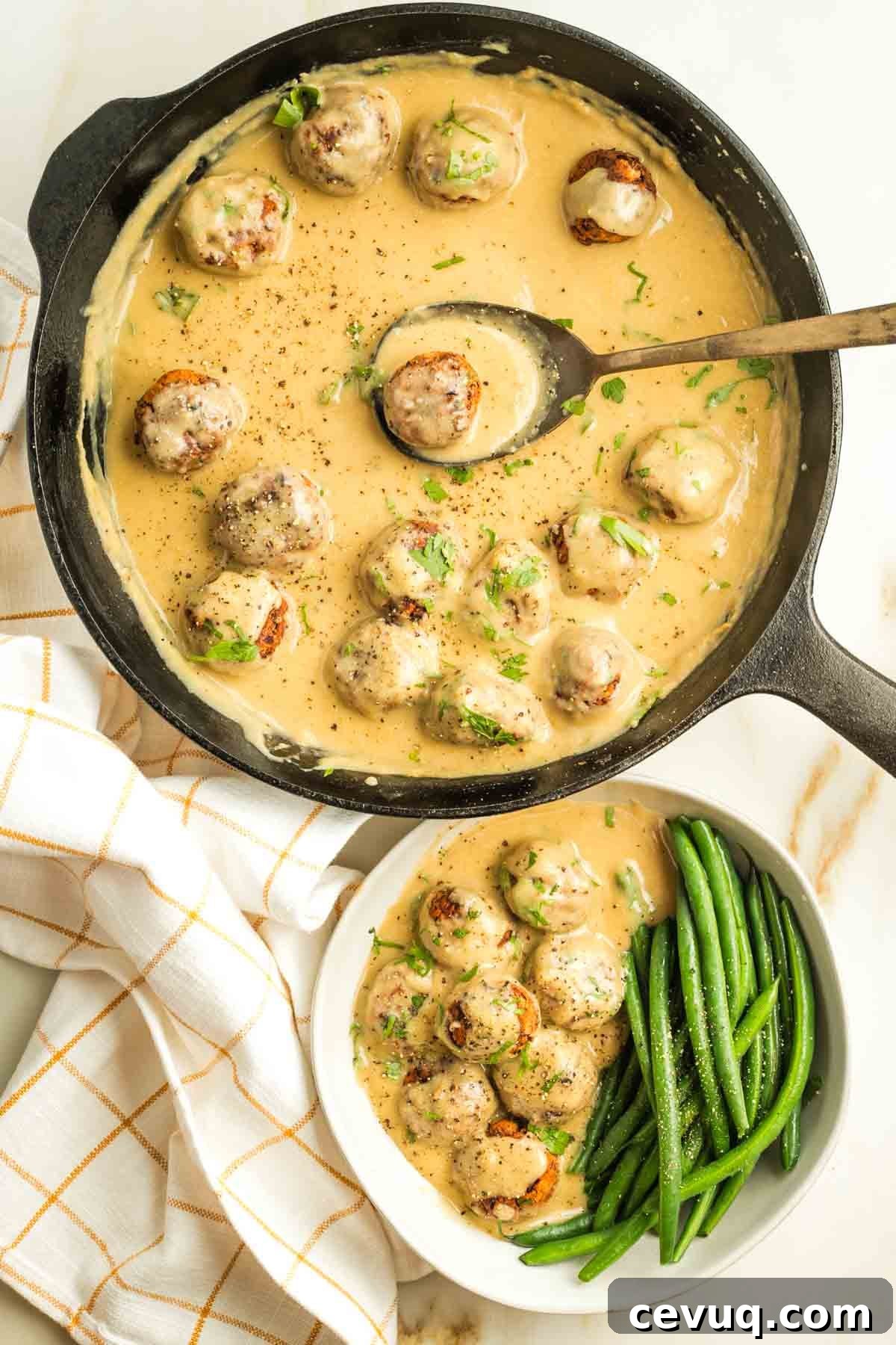 Cast iron skillet with a spoon scooping out a Swedish meatball in sauce and placing into a bowl with green beans and more meatballs in sauce.