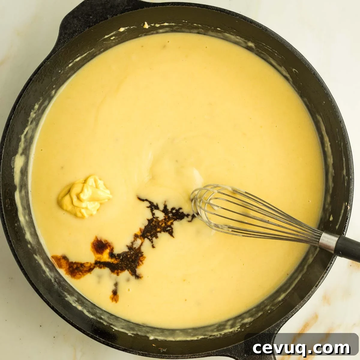A bit of dijon mustard and some tamari added to a yellow creamy sauce in a cast iron skillet.
