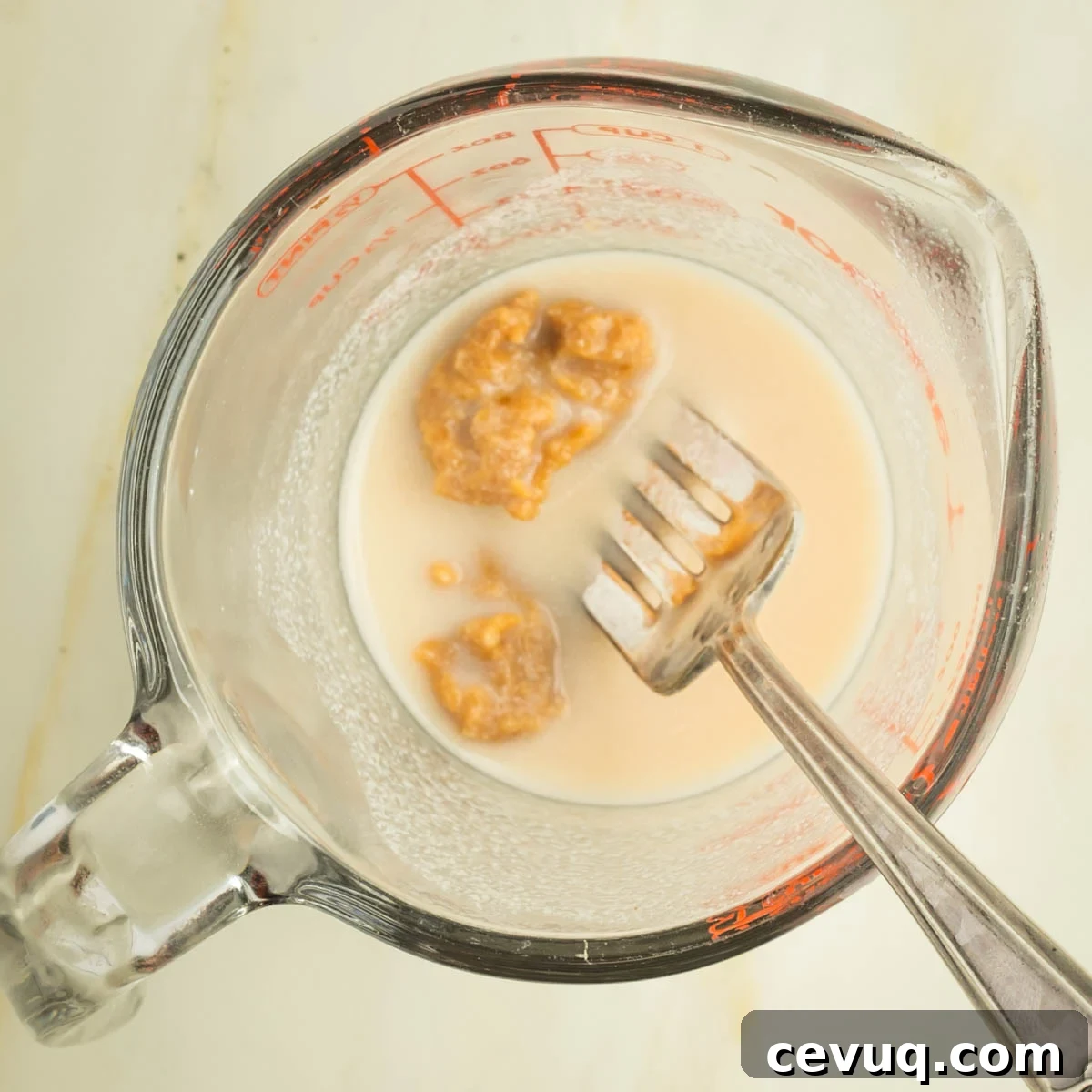 A fork mashing miso into some milk in a pyrex measuring cup.