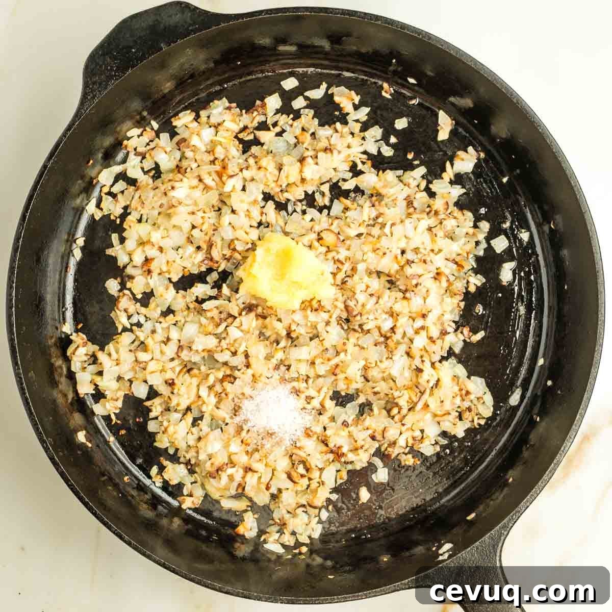 Sauteed onions and mushrooms in a cast iron skillet with grated garlic and salt on top.