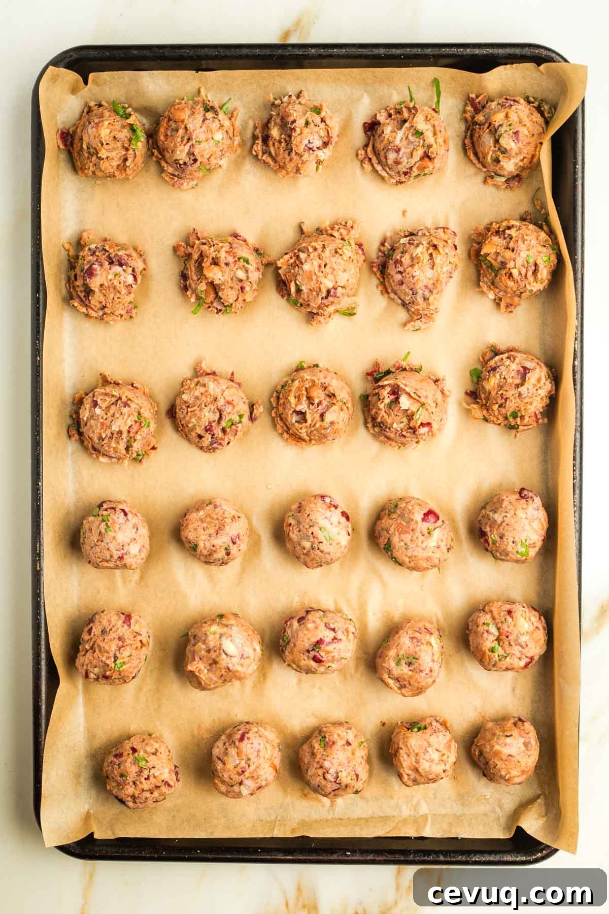 Small vegan Swedish meatballs in heaps on a baking sheet with parchment, half have been rolled into smooth balls.