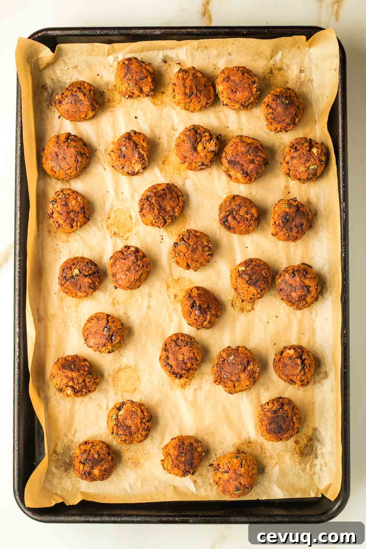 Baked  vegan Swedish meatballs on a tray lined with parchment paper.